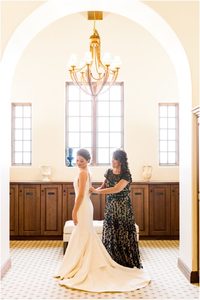 bride putting on dress with mom